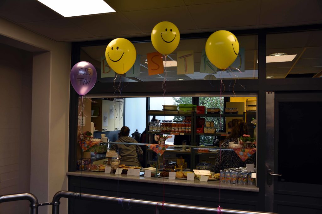 Cafeteria-Theke, darüber gelbe Smiley-Luftballons.
