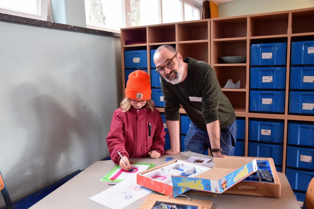 Lehrer und Schüler arbeiten an einem Tisch im Klassenraum.