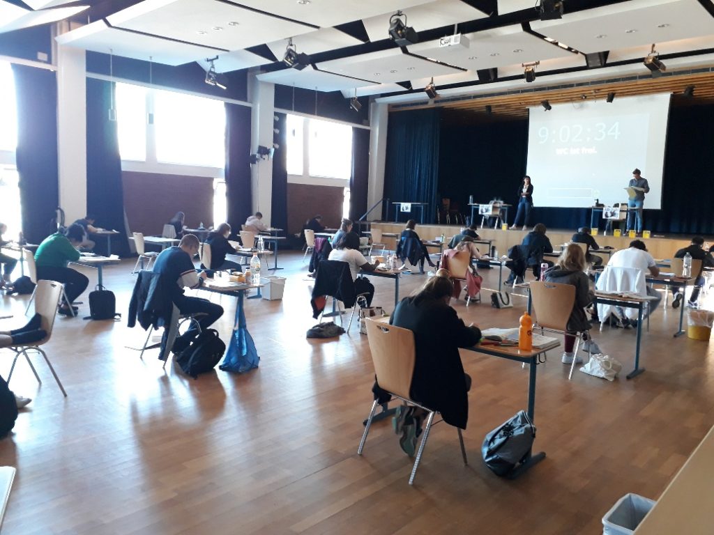 Schülerinnen und Schüler schreiben eine Prüfung in der Aula.