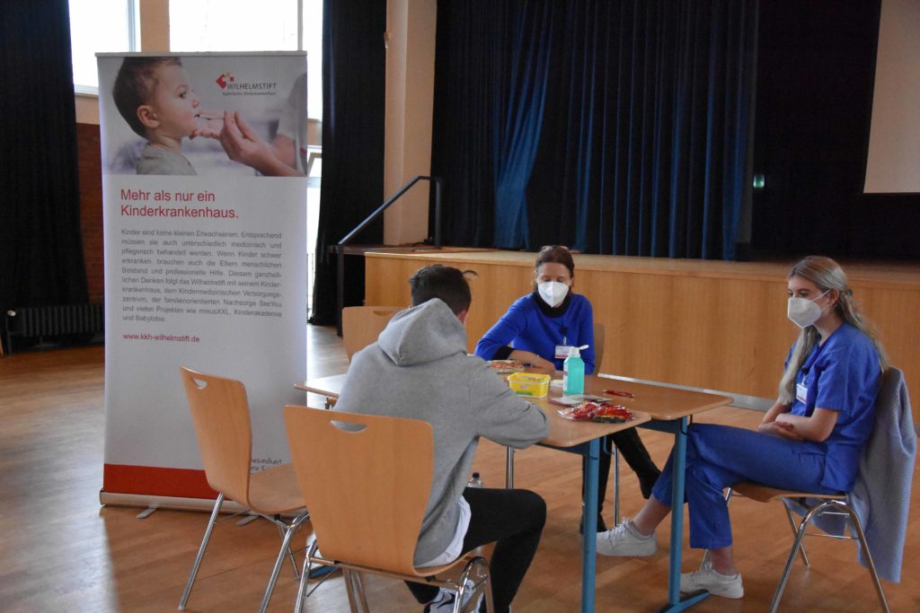 Gespräch an einem Stand mit Roll-up-Banner bei der Berufsmesse.