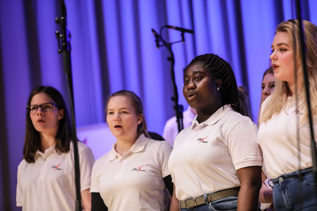 Sängerinnen in weißen Poloshirts singen auf der Bühne.