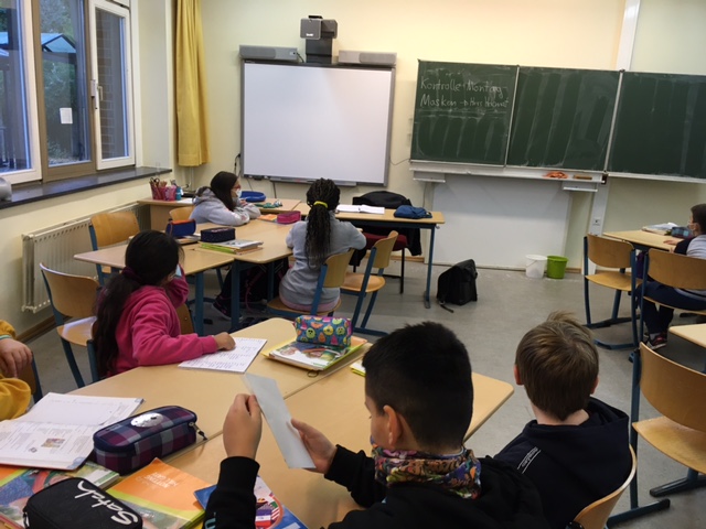 Kinder einer 5. Klasse sitzen an Tischen im Klassenraum.