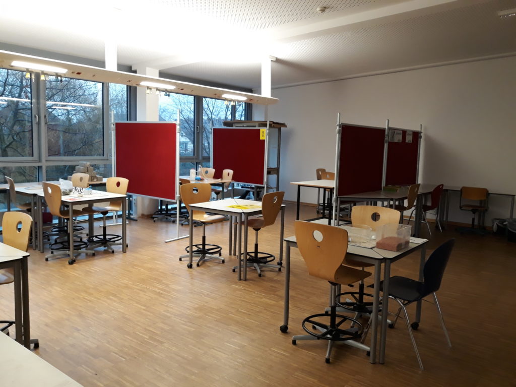 Klassenraum mit Gruppentischen und Stellwänden.