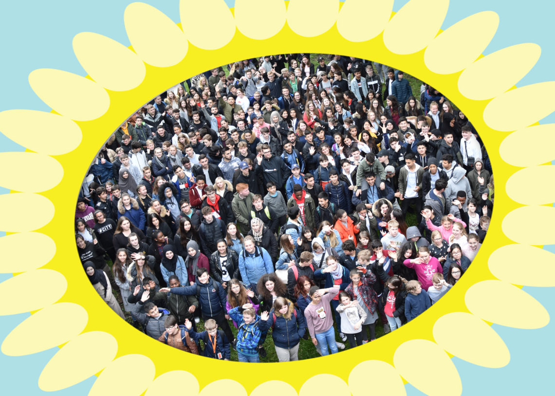Viele Schülerinnen und Schüler im Kreis einer gemalten Sonnenblume.