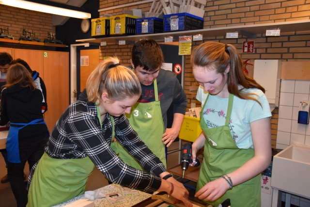 Schülerinnen und Schüler in grünen Schürzen arbeiten in der Holzwerkstatt.