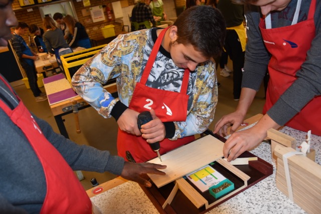 Schüler in Werkstattschürzen bearbeiten ein Werkstück an der Werkbank.