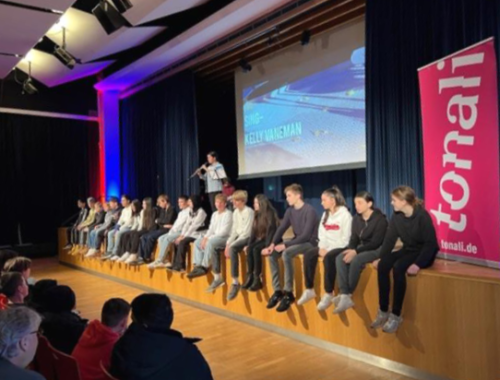 Gäste sitzen auf der Bühne der Aula bei einer Veranstaltung.