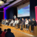 Gäste sitzen auf der Bühne der Aula bei einer Veranstaltung.