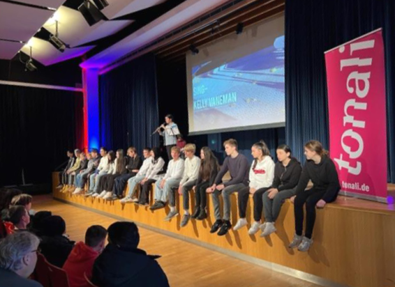Gäste sitzen auf der Bühne der Aula bei einer Veranstaltung.