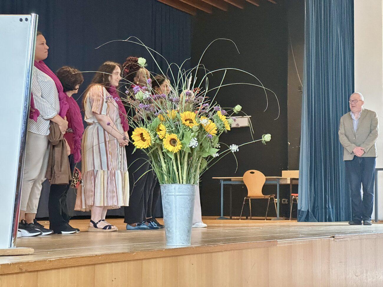 Begrüßung der neuen 5. Klassen auf der Bühne der Aula, vorne ein Strauß Sonnenblumen.