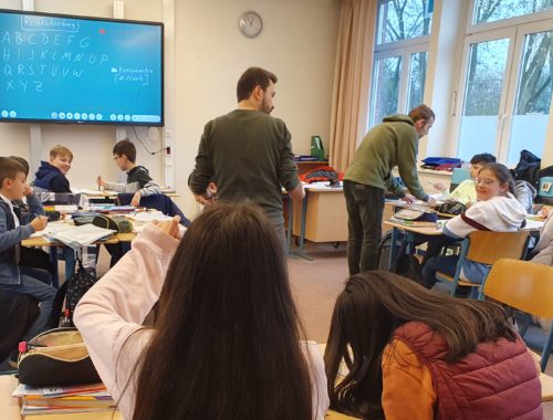 Schülerinnen und Schüler im Unterricht, vorne ein Bildschirm.