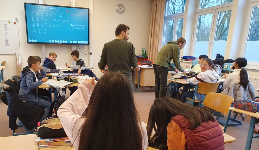 Schülerinnen und Schüler im Unterricht, vorne ein Bildschirm.