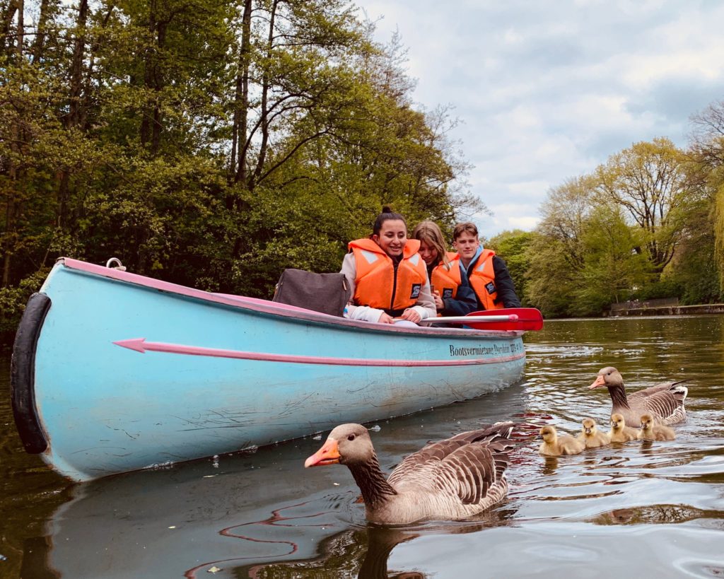 Kanu mit Schülerinnen und Schülern auf dem Wasser, vorne eine Entenfamilie.