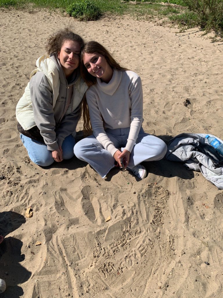 Zwei Schülerinnen sitzen im Sand am Elbstrand.