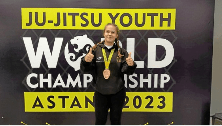 Jette Kuhn mit Medaille vor dem Banner der Ju-Jitsu Youth World Championship 2023 in Astana.