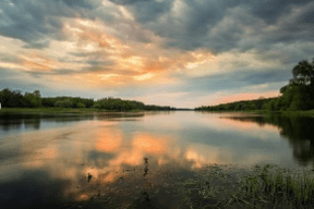 Sonnenuntergang über einem ruhigen Fluss, in dem sich die Wolken spiegeln.