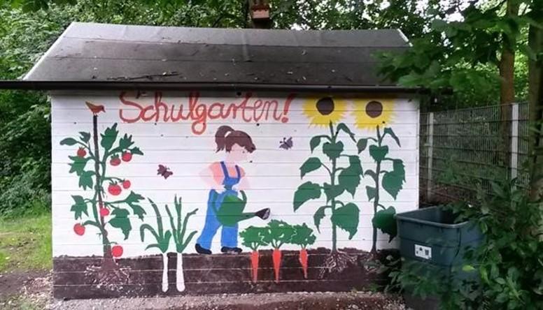 Bemalte Gartenhütte mit der Aufschrift „Schulgarten“ und gemalten Blumen.