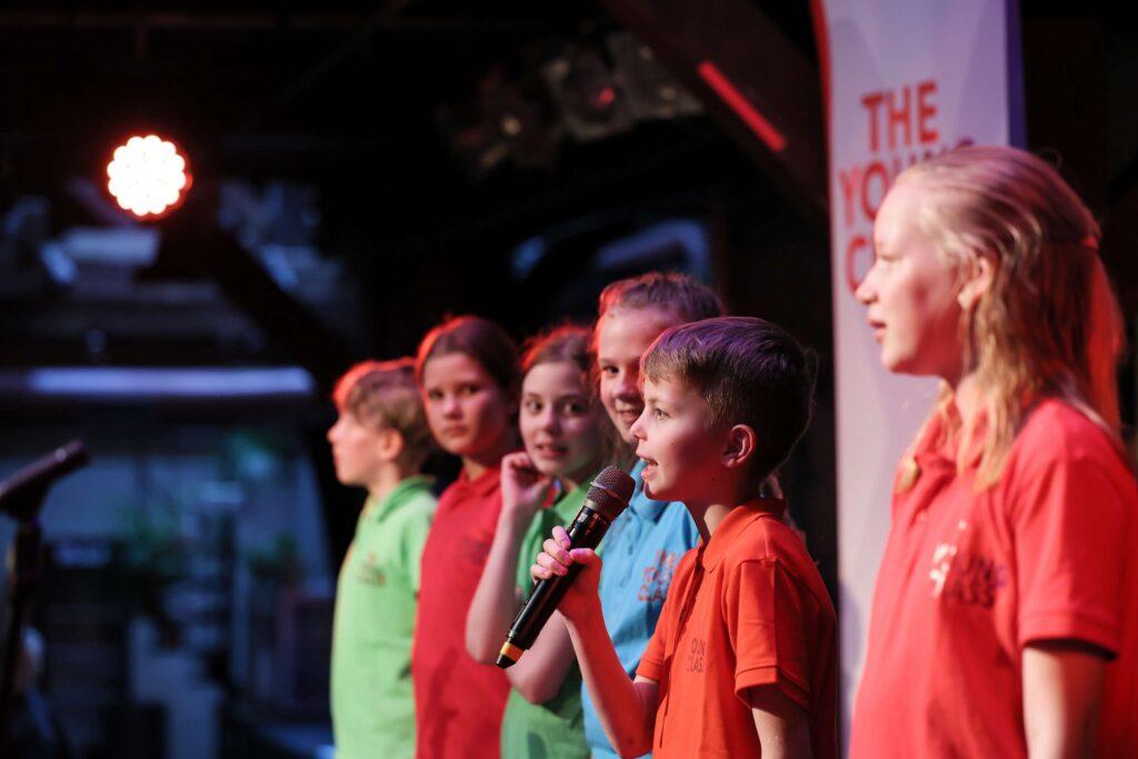 Junge Sängerinnen und Sänger in bunten T-Shirts beim Konzert in der Fabrik.