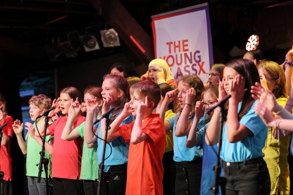 Unterstufenchor in bunten T-Shirts auf der Bühne der Fabrik.