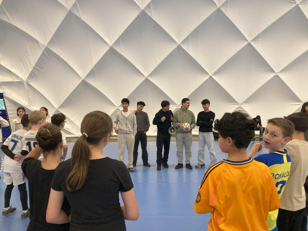Schülergruppe in einer Sporthalle mit gewölbter Decke.