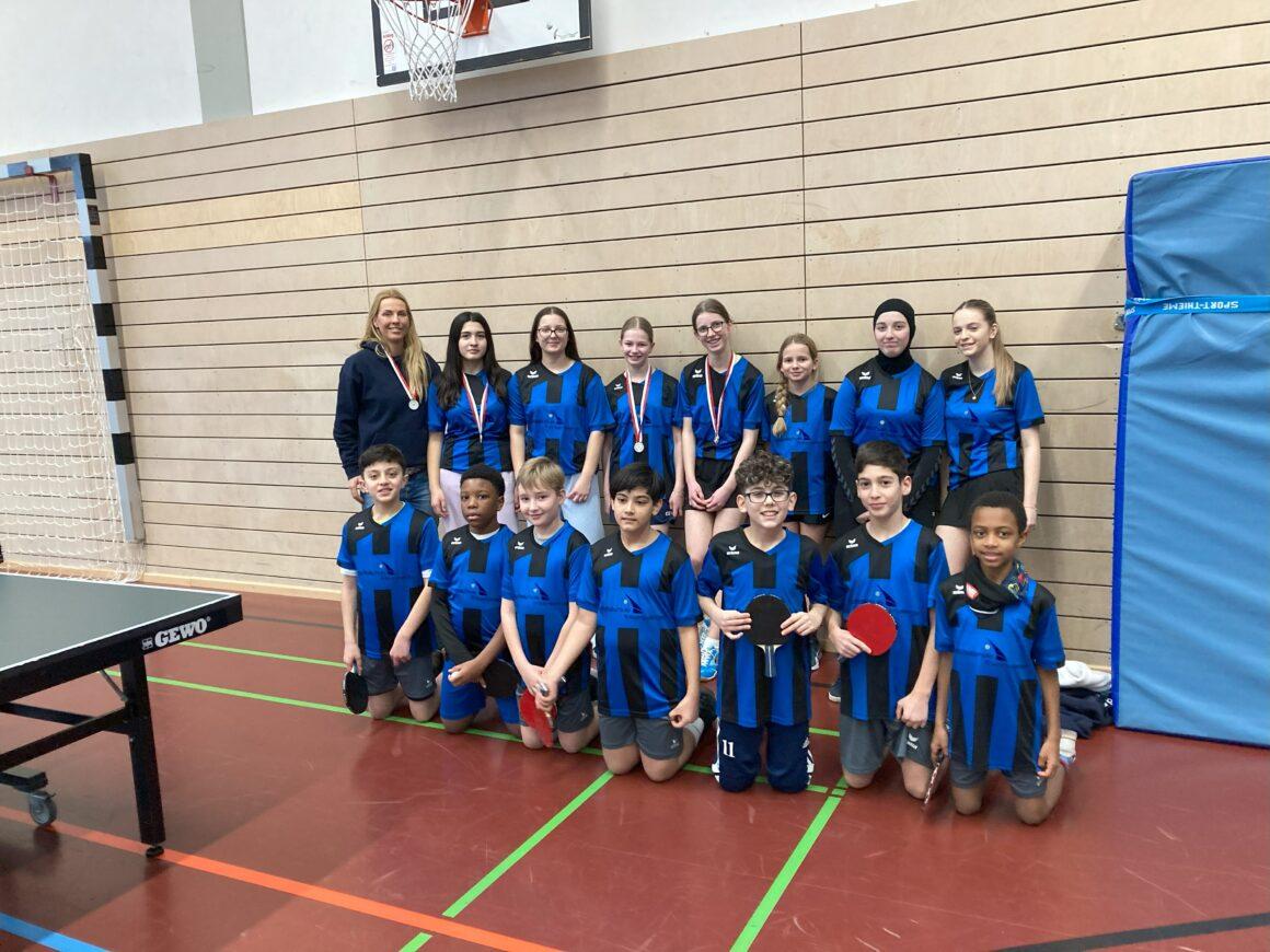 Zwei Tischtennismannschaften in blauen Trikots in der Sporthalle.