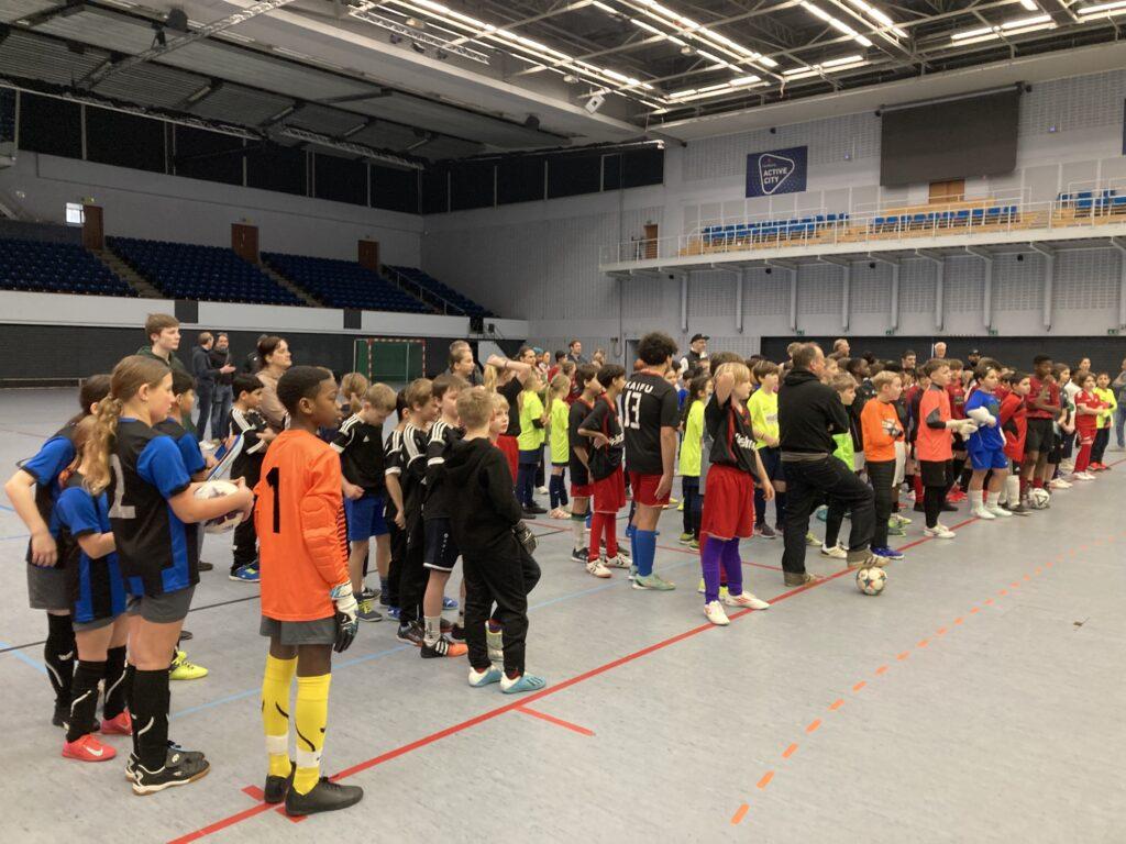Mannschaften stellen sich in einer großen Sporthalle auf.