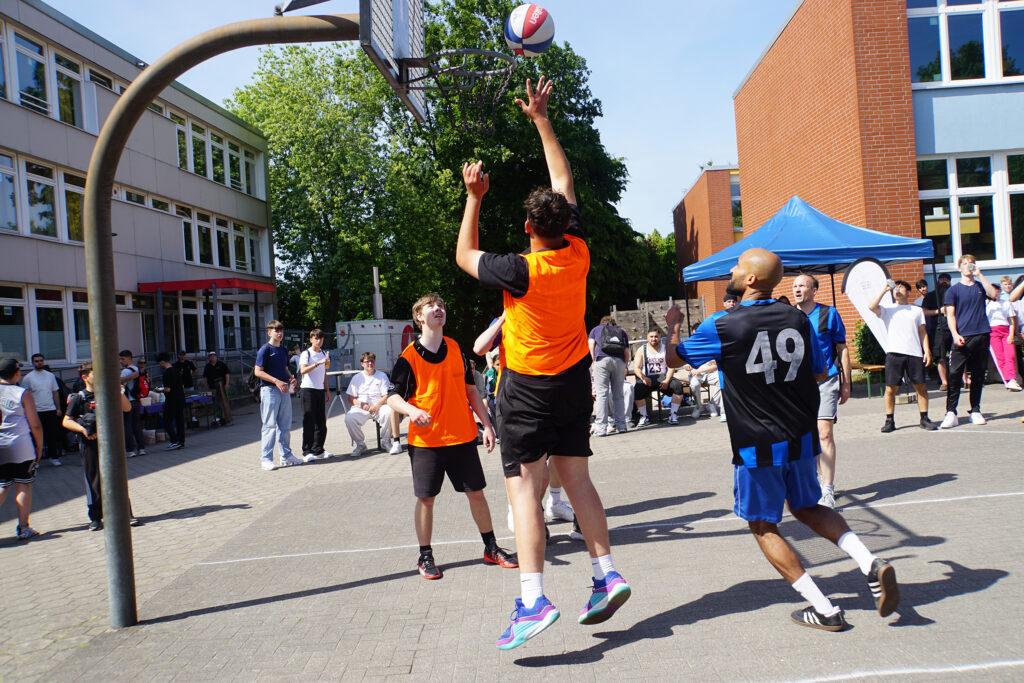 Streetball-Spiel auf dem Schulhof vor vielen Zuschauenden.