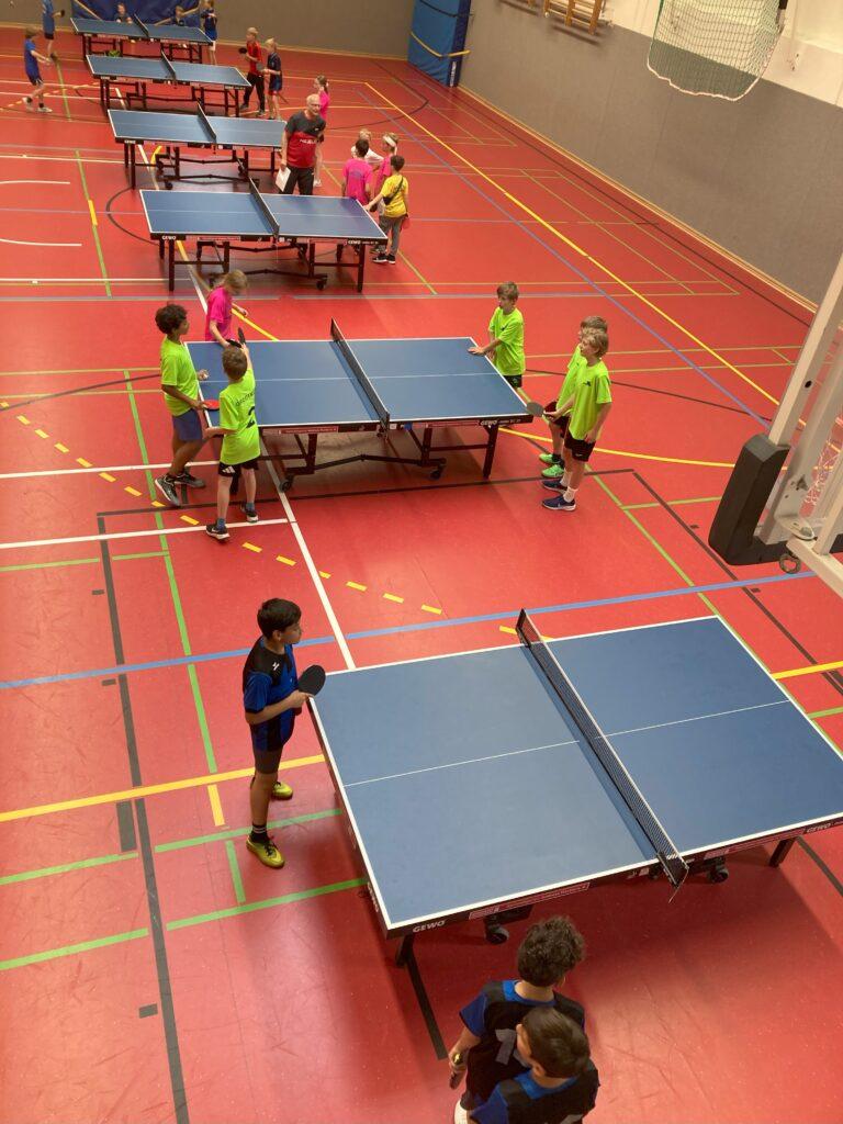Tischtennisspiele an mehreren Platten in einer Sporthalle.