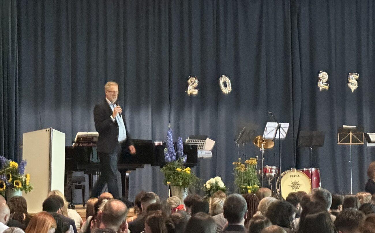 Rede auf der Bühne bei der Abschlussfeier des Jahrgangs 10, im Hintergrund die Zahl 2025.
