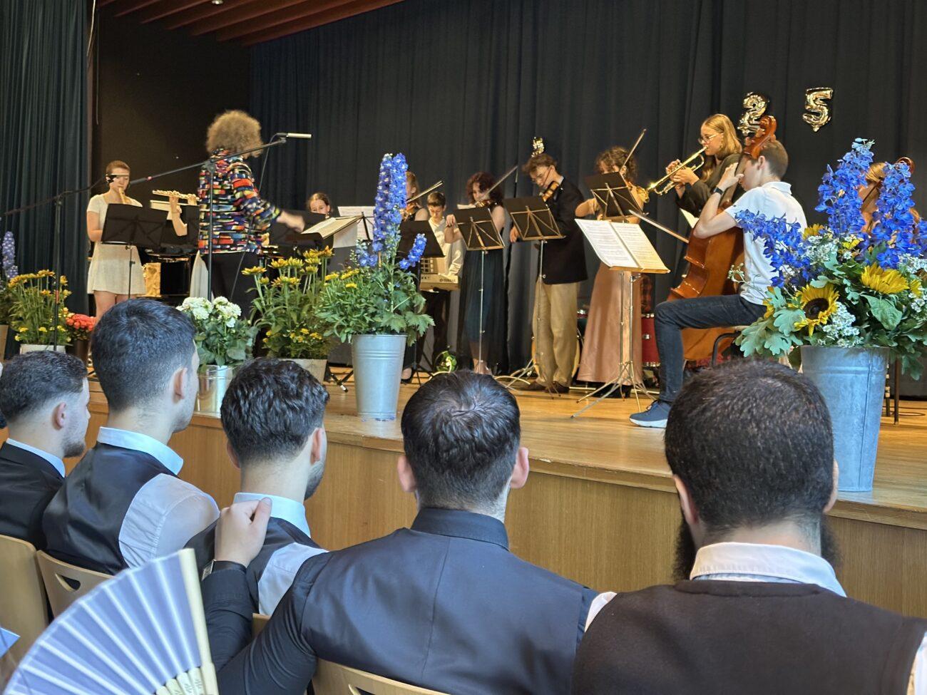 Abiturfeier: Gäste in der festlich geschmückten Aula, auf der Bühne Musikerinnen.