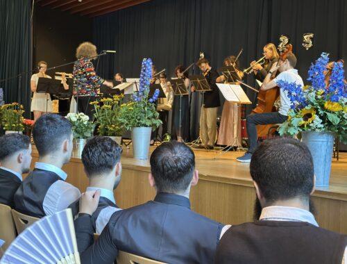 Abiturfeier: Gäste in der festlich geschmückten Aula, auf der Bühne Musikerinnen.