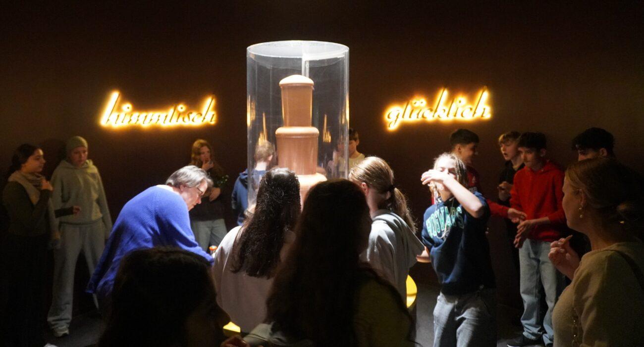 Schülerinnen und Schüler betrachten in einer abgedunkelten Ausstellung eine Vitrine.