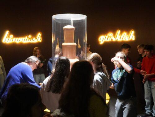 Schülerinnen und Schüler betrachten in einer abgedunkelten Ausstellung eine Vitrine.