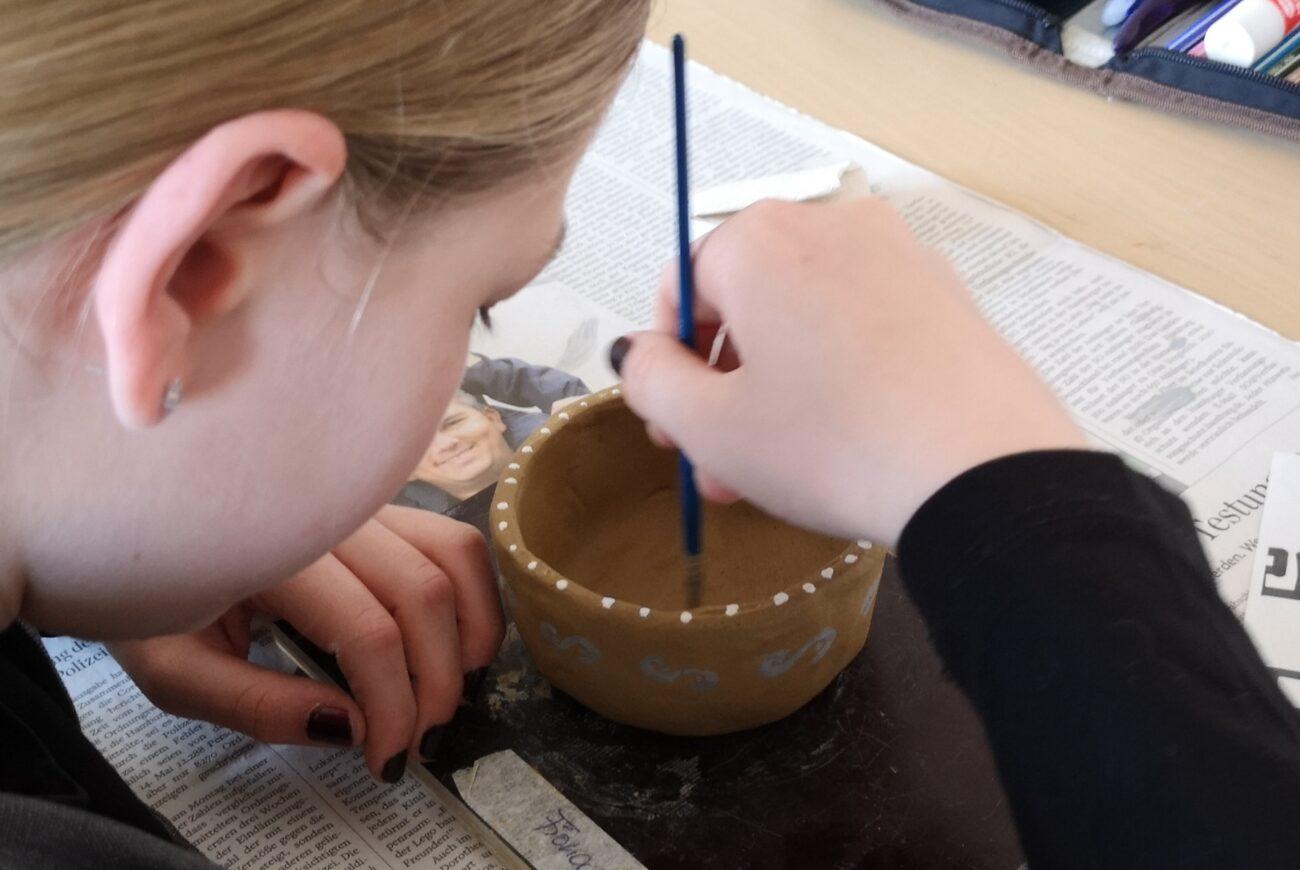 Schülerin bemalt eine selbst getöpferte Schale mit dem Pinsel.
