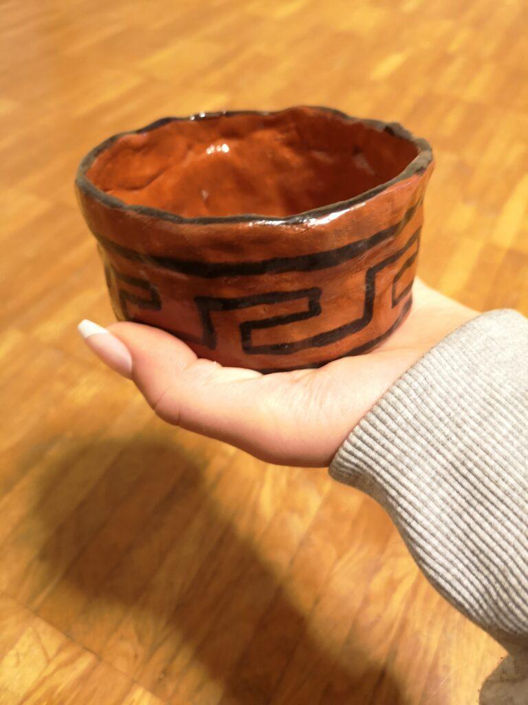 Hand hält eine selbst getöpferte, bemalte Schale.