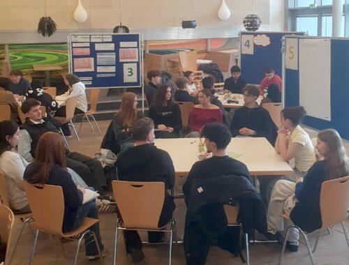 Informationsveranstaltung im Worldcafé-Format: Gruppen sitzen an Tischen in der Mensa.