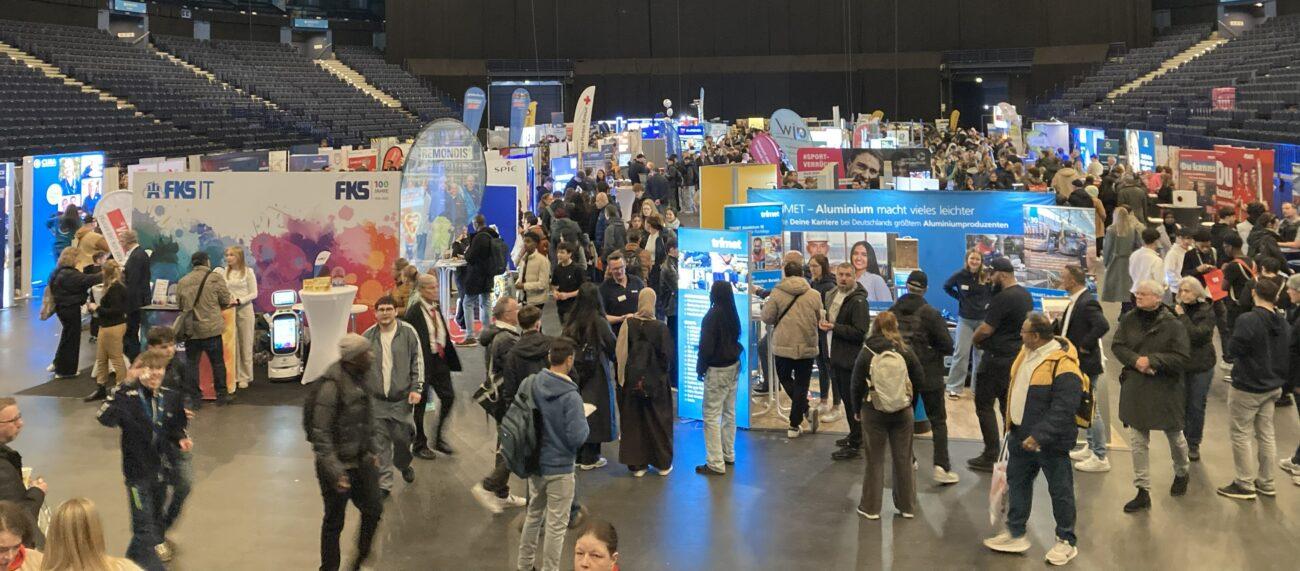 Jugendliche besuchen eine große Jobmesse mit vielen Ständen.