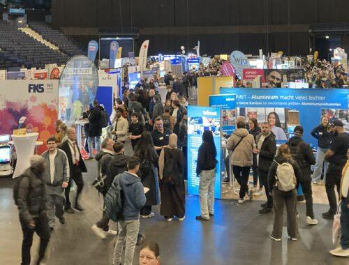 Jugendliche besuchen eine große Jobmesse mit vielen Ständen.