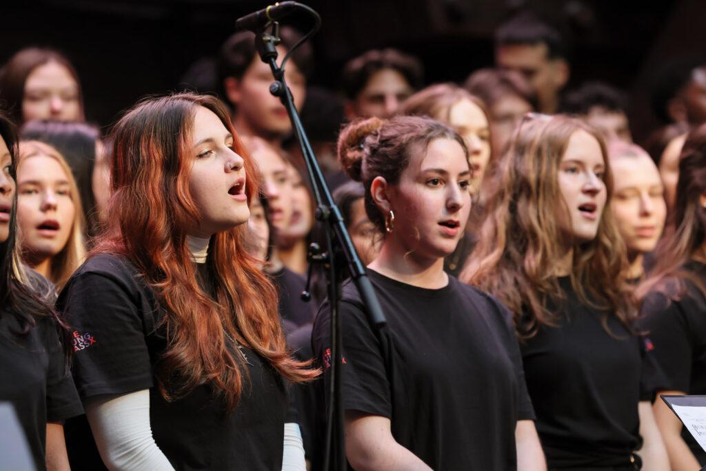 Sängerinnen in schwarzen T-Shirts singen im Chor.