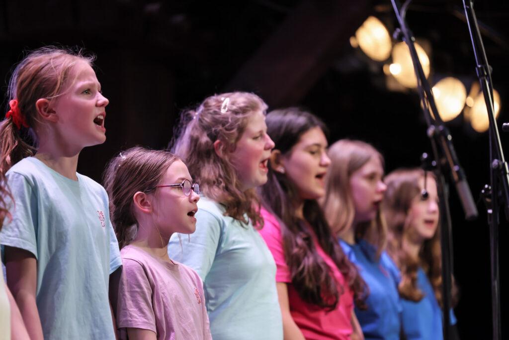Jüngere Sängerinnen in bunten T-Shirts singen auf der Bühne.