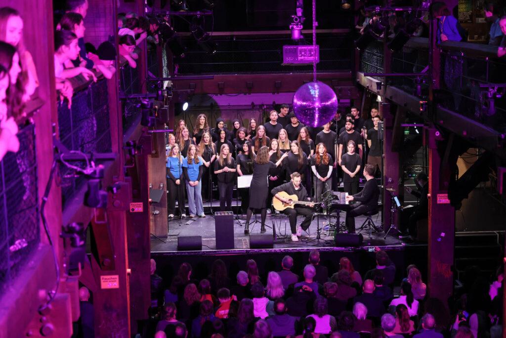 Chor mit Band auf der Bühne beim Stadtteilkonzert, violettes Licht.