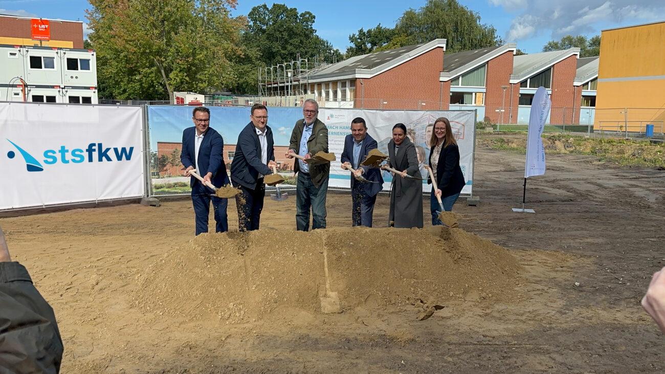 Spatenstich für die neue Sporthalle: Gäste mit Spaten auf der Baufläche vor der Schule.