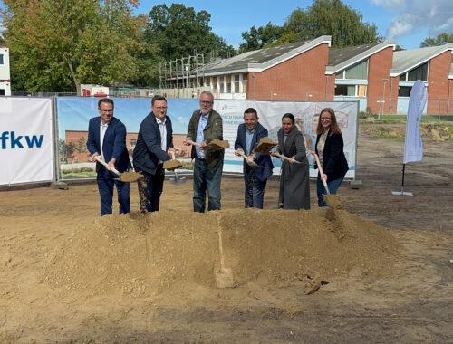 Spatenstich für die neue Sporthalle: Gäste mit Spaten auf der Baufläche vor der Schule.